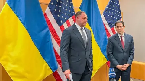 Reuters Andriy Yermak and Marco Rubio stand in front of Ukrainian and US flags in a conference room. Yermak is wearing a grey tie, and Rubio a red one.