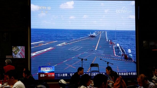 FILE PHOTO: Customers dine near a giant screen broadcasting news footage of an aircraft taking off from Chinas Shandong aircraft carrier while taking part in a combat readiness patrol and Joint Sword exercises around Taiwan conducted by the Eastern Theatre Command of Chinas Peoples Liberation Army (PLA), at a restaurant in Beijing, China April 10, 2023.