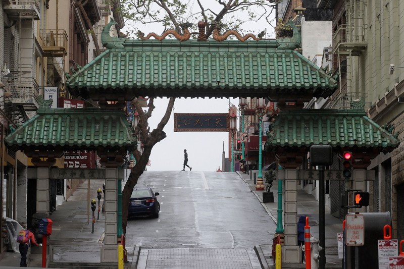 Pedestrian crosses the street behind the Dragon Gate, an entrance to Chinatown in San Francisco