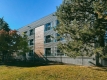 The outside wall of the three-story building is set behind trees and a construction fence during a clear, sunny day.