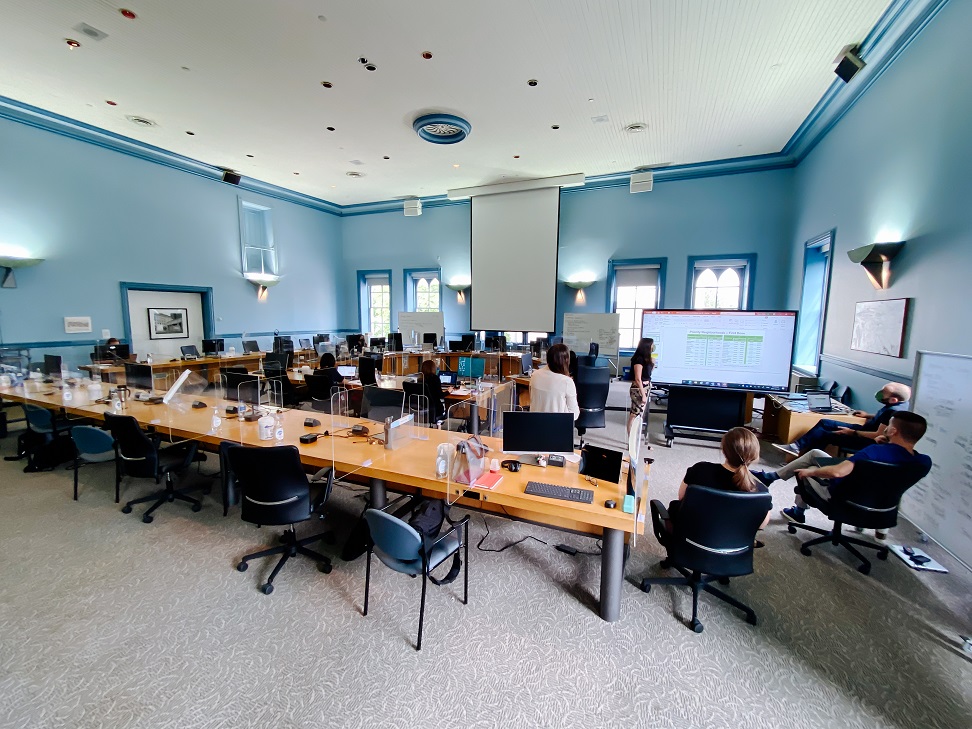 Five people meet in front of a large screen in the corner of the Champlain room