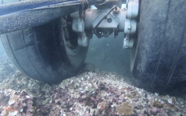 In this image taken from video provided by the U.S. Navy, Navy divers assigned to Mobile Diving and Salvage Unit One (MDSU-1) conduct an underwater survey of the U.S. Navy's P-8A Poseidon in Kaneohe Bay, Hawaii, on Tuesday, Nov. 28, 2023. The U.S. Navy said the underwater footage shows two points where the large plane is touching coral in the Hawaii bay. It's been more than a week since the Navy plane overshot a runway and landed in shallow water just offshore of Marine Corps Base Hawaii at Kaneohe Bay. (U.S. Navy via AP)