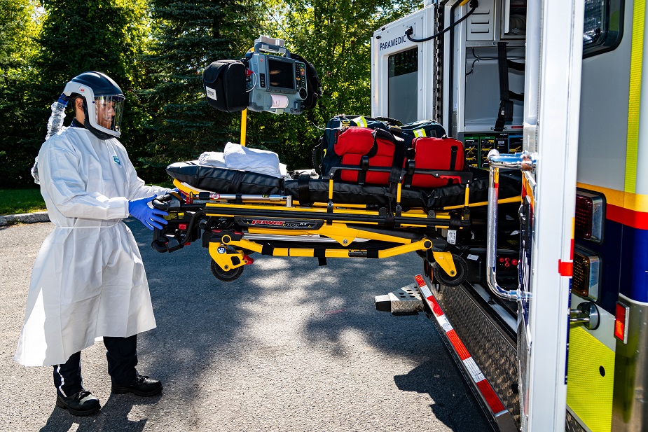 Paramedic wearing protective clothing and loading a stretcher into an ambulance