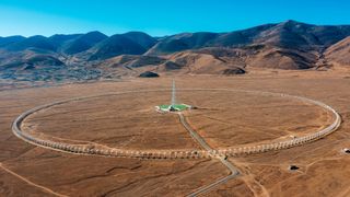 a white tower surrounded by a ring of objects in a desert mountain landscape