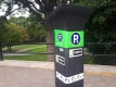 A City of Ottawa parking pay and display machine with a green space filled with trees in the background. 