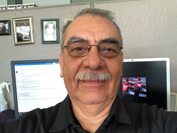 A man with glasses and a moustache sitting at a desk in front of a computer