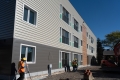 Three people in safety equipment walk alongside the exterior of three three-story building that is under construction.