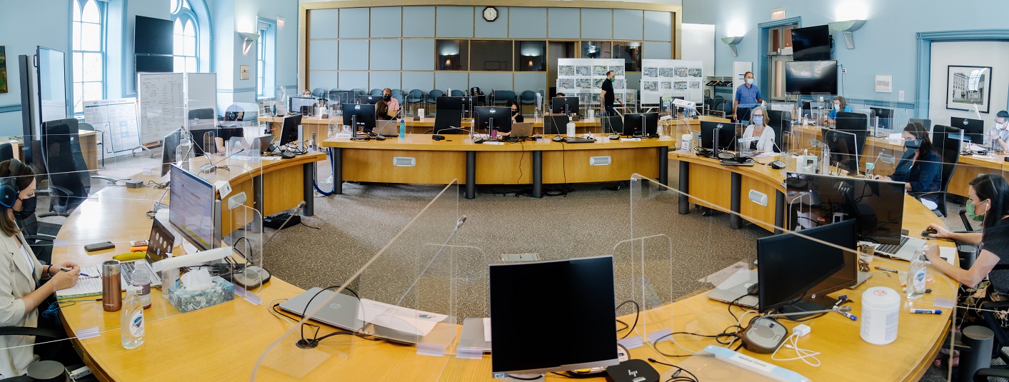 The Champlain meeting room with desks, computers, plexiglass barriers and a dozen people sitting apart from each other