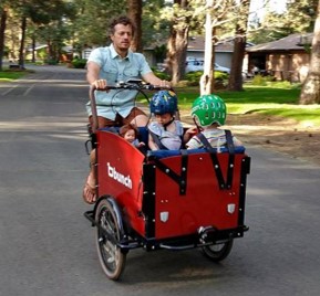 A man using a personal e-cargo bike to transport two children.