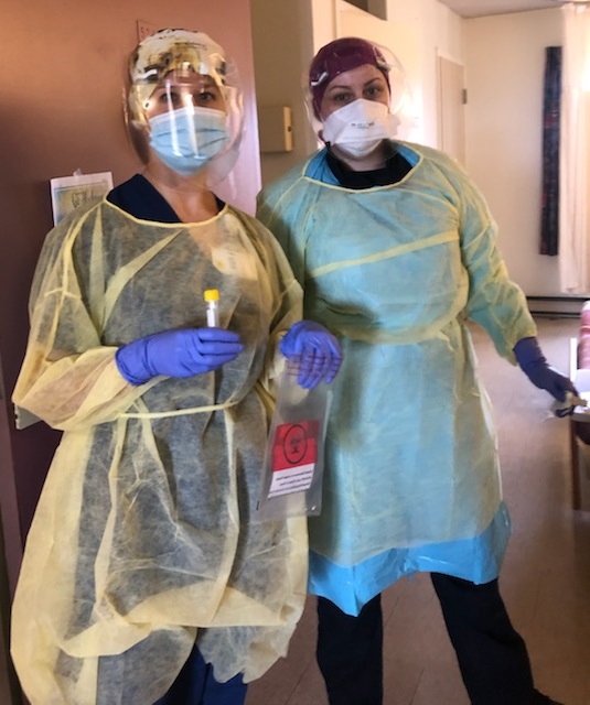 Two women wearing medical gowns, masks and gloves