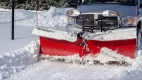 A pickup truck equipped with a v-plow clearing snow from a driveway.