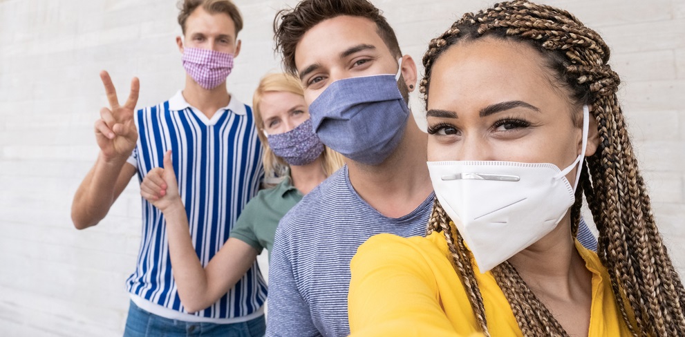 Four young adults wearing masks and taking a group selfie..