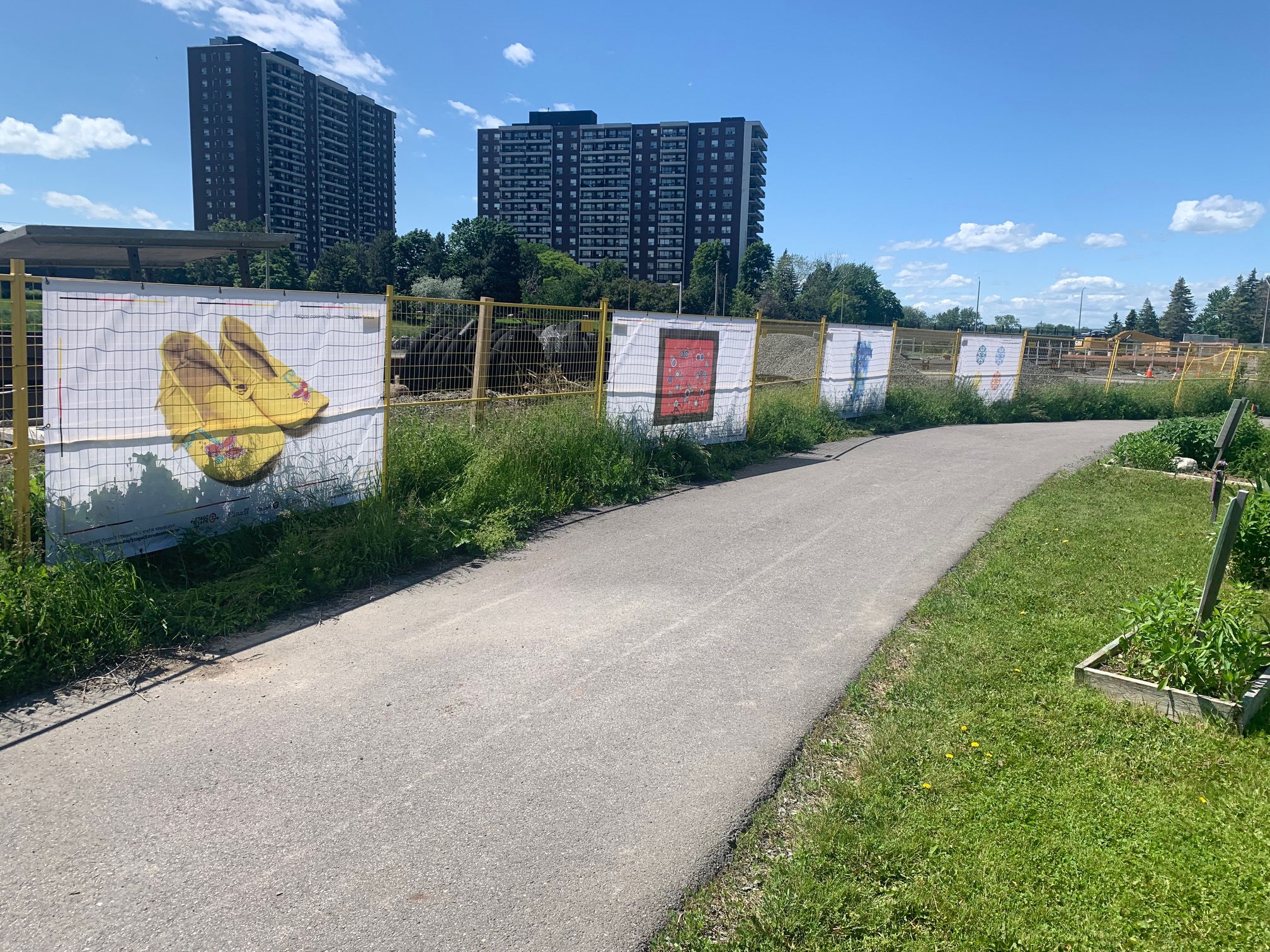 Artwork hanging on construction fencing in front of a public pathway