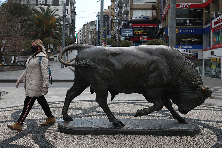 A woman, wearing a mask and gloves walks by a statue in Istanbul, Friday, April 3. 