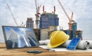 A computer screen, phone and tablet with a construction helmet, drafting paper and a building under construction