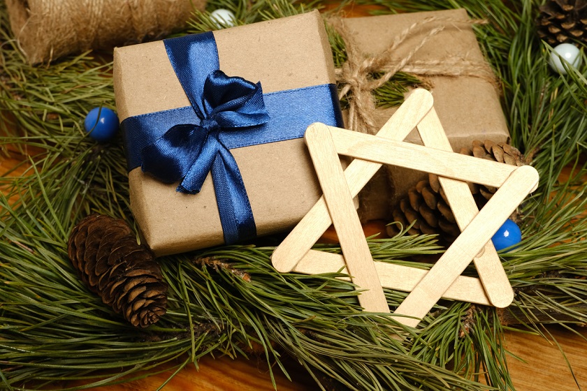 A Star of David made of popsicle sticks and some cardboard packages placed on top of an arrangement of fir branches and pinecones.