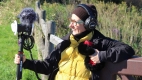 A smiling person holding a binaural microphone at the Monahan Wetlands.