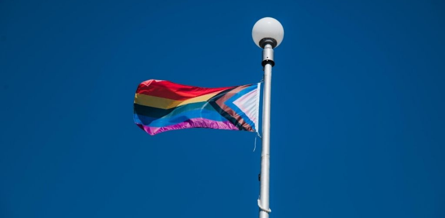 A flag pole with a Pride flag waving in the wind.