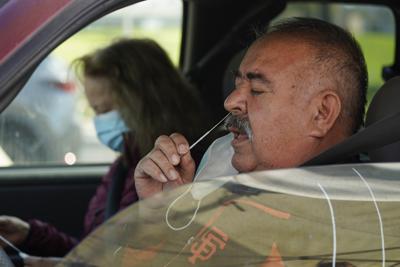 FILE - Jose Alfrtedo De la Cruz and his wife, Rogelia, self-test for COVID-19 at a No Cost COVID-19 Drive-Through event provided the GUARDaHEART Foundation for the City of Whittier community and the surrounding areas at the Guirado Park in Whittier, Calif., on Tuesday, Jan. 25, 2022.  Omicron, the highly contagious coronavirus variant sweeping across the country, is driving the daily American death toll higher than during last fall's delta wave, with deaths likely to keep rising for days or even weeks. (AP Photo/Damian Dovarganes)