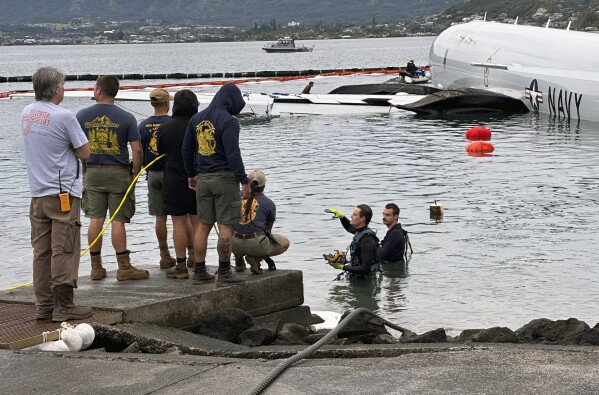 Contractors place inflatable bags under a U.S. Navy P-8A in Kaneohe Bay, Hawaii, Friday, Dec. 1, 2023, so they can float the aircraft over the water and onto land. The Navy plans to use inflatable cylinders to lift the jet off a coral reef and then roll it over to a runway to remove the plane from the ocean where it crashed the week before. (AP Photo/Audrey McAvoy)