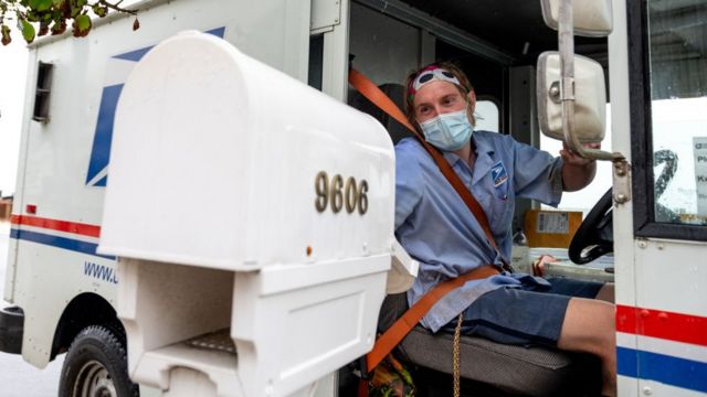 A postal worker delivers mail wearing a mask