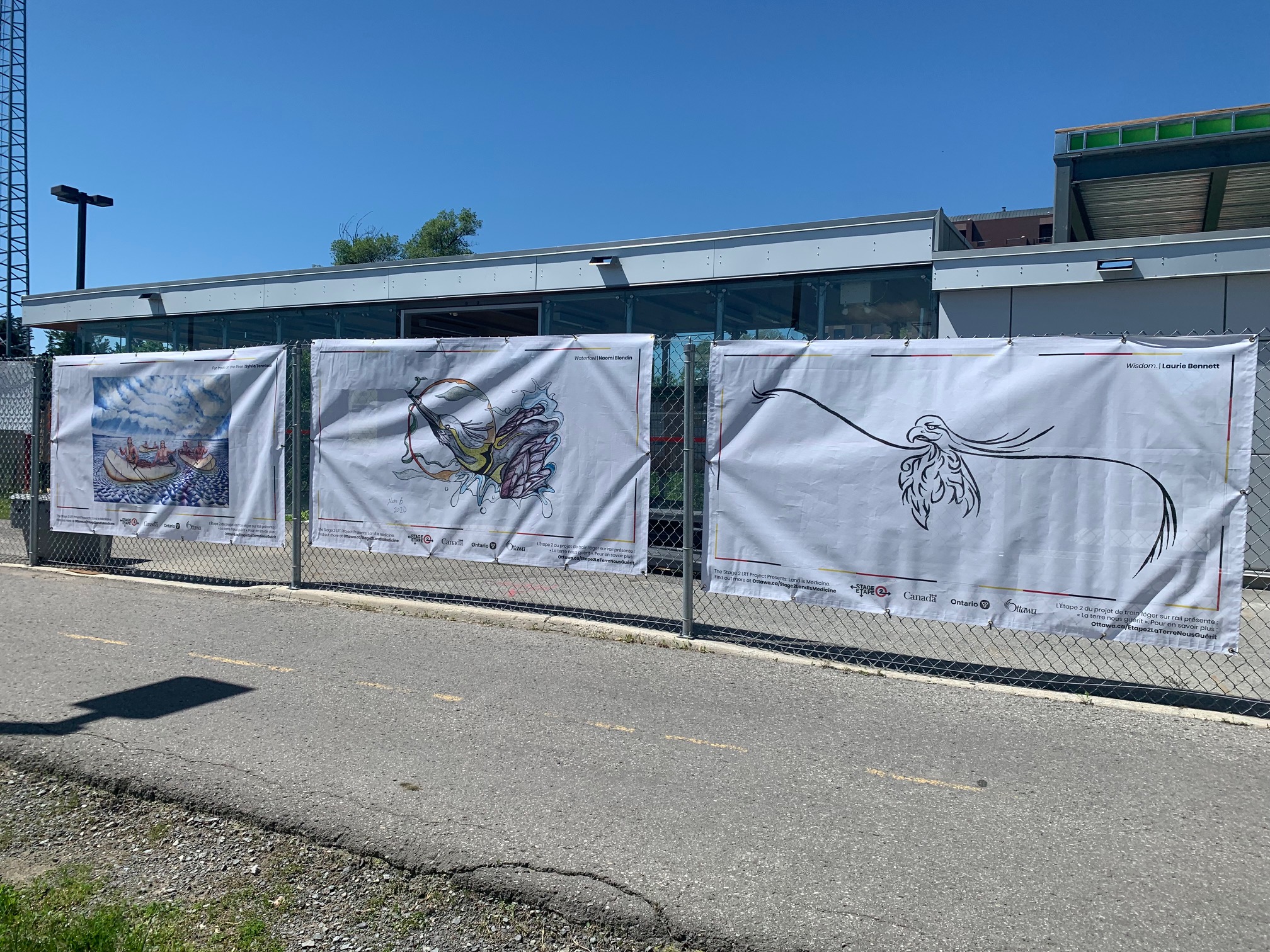 Artwork hanging on construction fencing in front of a public pathway