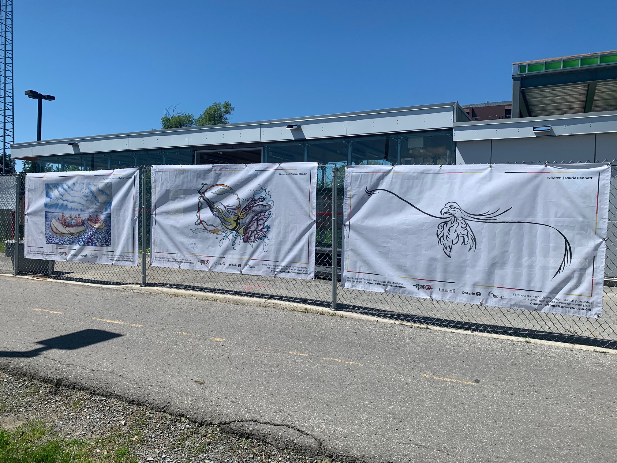 Artwork hanging on construction fencing in front of a public pathway