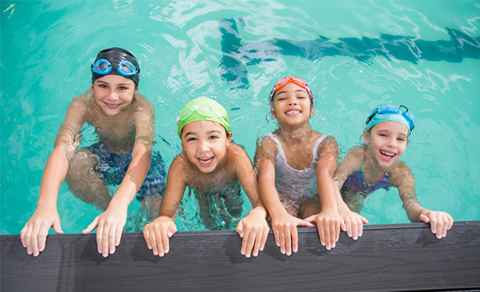 Four smiling children hanging off the edge of a pool