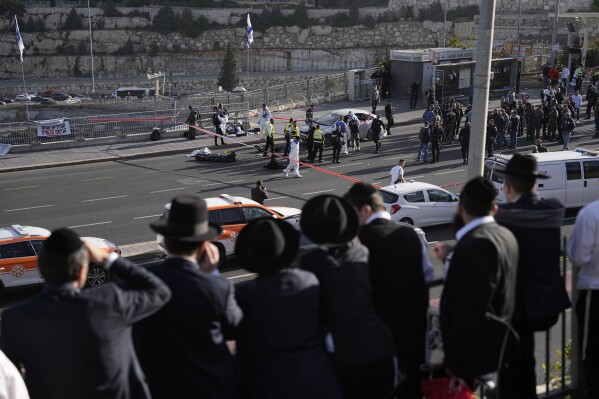 FILE - People look at Israeli police officers and volunteers from the Zaka rescue service work at the shooting attack in Jerusalem, Thursday, Nov. 30, 2023. The shooting death of an Israeli man who raced to confront Palestinian attackers has raised questions about the use of excessive force among Israeli security forces and the public. The man's shooting mirrors previous incidents where Israeli security forces or civilians have opened fire on attackers who no longer appear to pose a threat or on suspected assailants or unarmed civilians. (AP Photo/Ohad Zwigenberg, File)