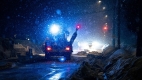 A snow plow, in the dark, with its lights on plowing a street while it is snowing. / Un chasse-neige éclairant de ses feux la rue à déneiger dans la nuit.