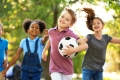 A child holding a soccer ball runs forward  followed by other children.